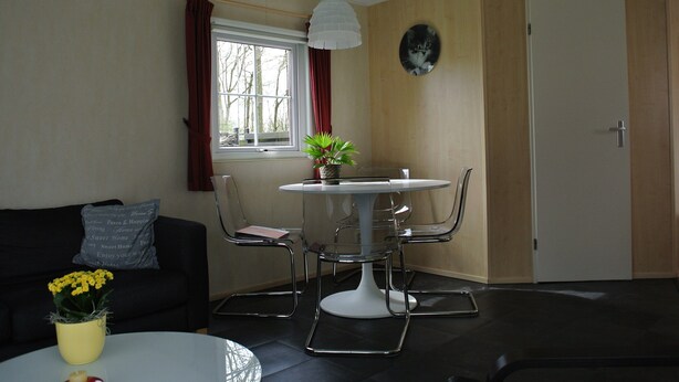Un salon avec une table ronde, des chaises, un canapé, une plante en pot et une fenêtre avec des rideaux.