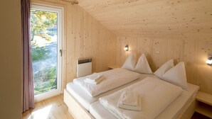 A wooden room with a bed, a window with curtains, and a wall-mounted heater. - Chalet With Indoor hot tub (Sankt Georgen am Kreischberg)