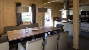 A dining area with a wooden table and chairs, a window with curtains, and a view of the outside. - Chalet With Indoor hot tub (Sankt Georgen am Kreischberg)