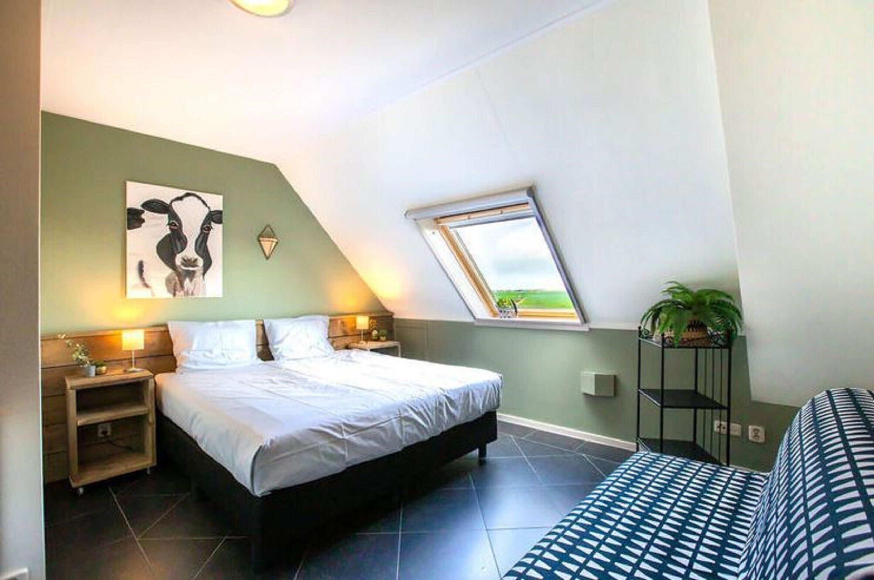A bedroom with a bed, a nightstand, a window, and a plant.