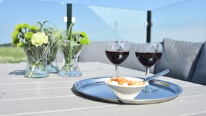 Une table avec deux verres de vin rouge, un bol de noix et un plateau sur une terrasse extérieure.