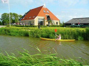A building with a red roof and a yellow canoe on a river. - Farm Located in a Beautiful Area of Friesland (Lollum)