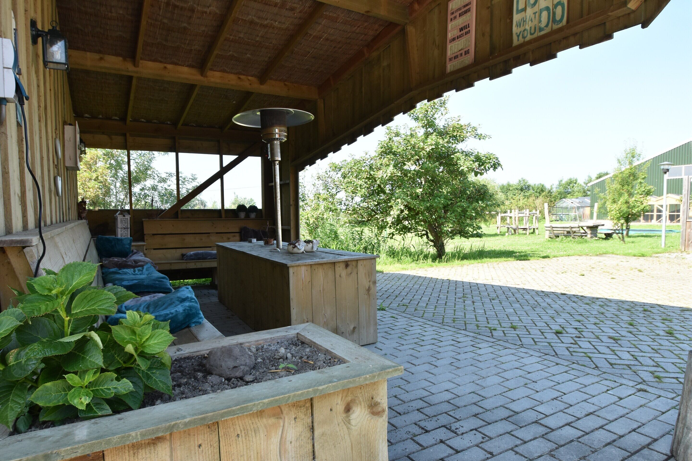A wooden outdoor seating area with a table and benches, a planter with green plants, and a metal lamp post.