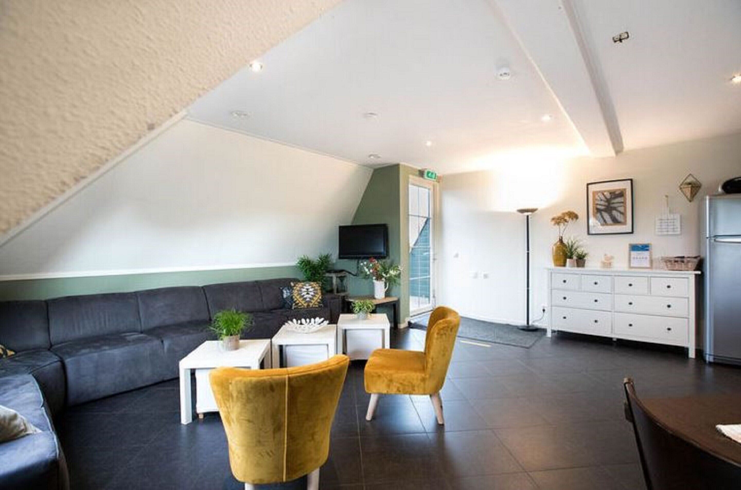 A modern living room with a dark grey sectional sofa, a yellow armchair, a white coffee table, and a flat-screen TV.