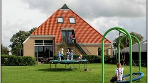 Une maison avec un toit recouvert de tuiles rouges, un porche à l’avant et une balançoire dans le jardin.