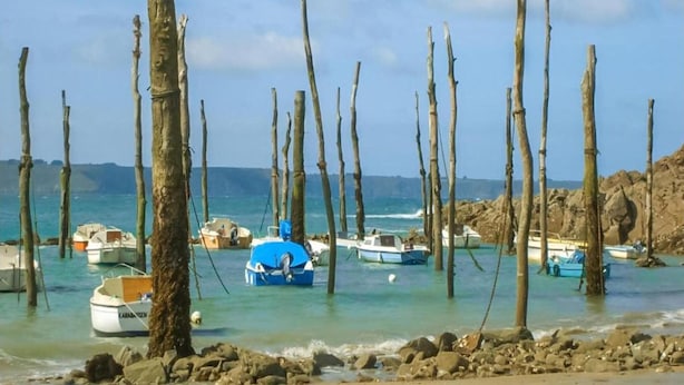 Een strand met houten palen, boten en rotsachtig terrein.