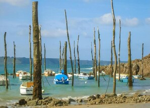 Una playa con postes de madera, barcos y terreno rocoso.