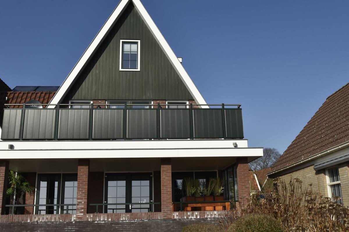 Ein modernes, zweistöckiges Haus mit markantem Giebeldach, großen Fenstern und einem Balkon.
