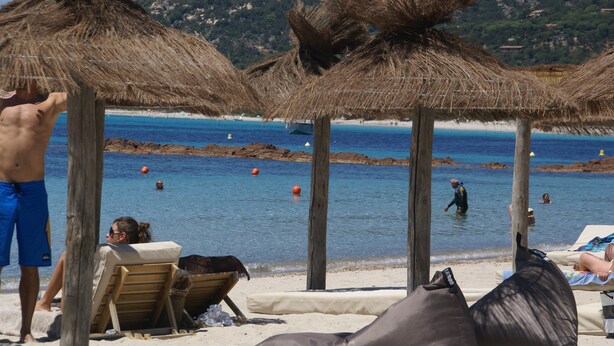 Une plage bordée de parasols en chaume, une plage de sable fin et une mer d’un bleu limpide.
