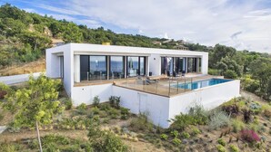 Une maison moderne dotée d’une piscine, de grandes fenêtres et offrant une vue sur les collines environnantes.