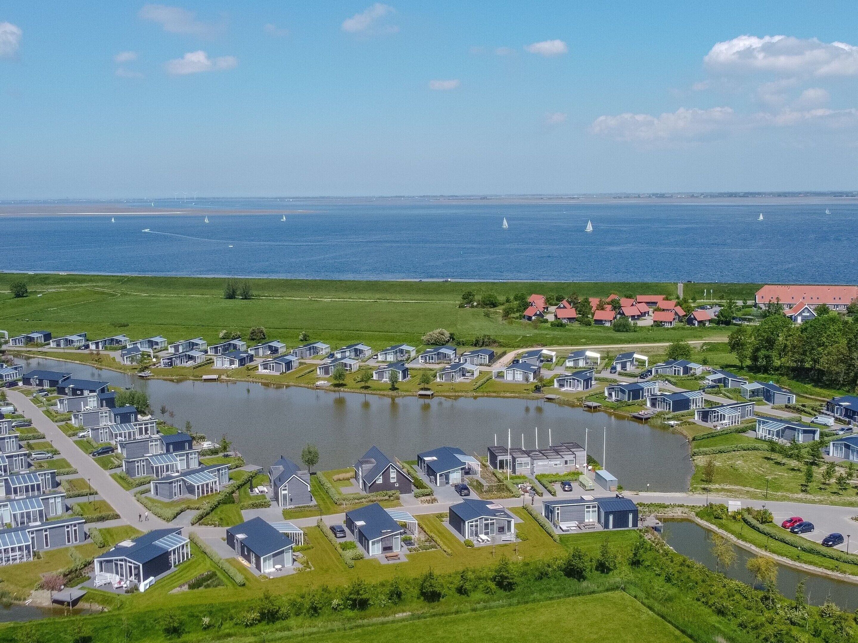 Zona residencial junto al lago con casas modernas, un estanque central y vistas al mar con veleros.