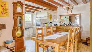 A kitchen with wooden beams, a dining table with chairs, a large clock, and a chandelier. - Beachside Family Retreat (Penestin)