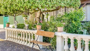 A bench with a railing, surrounded by potted plants and greenery. - Beachside Family Retreat (Penestin)