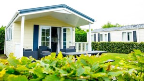 Ein Bungalow mit Veranda, einer kleinen Terrasse und einem Garten im Vordergrund.