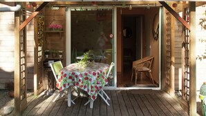 Eine Holzterrasse mit Tisch und Stühlen, eine Glastür zum Innenbereich und eine hölzerne Pergola darüber.