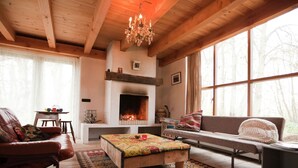 Un salon chaleureux avec une cheminée, des poutres en bois, un canapé, un banc et un tapis.
