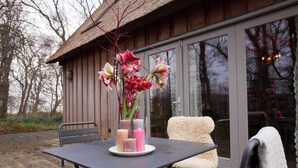 Une table décorée de bougies et de fleurs est placée sur une terrasse, d’où l’on peut admirer un bâtiment en bois doté de grandes fenêtres.