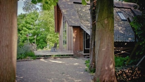 Un chalet rustique avec une allée en gravier, une terrasse en bois et un espace extérieur aménagé et abrité.