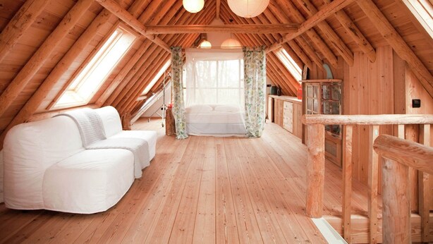 Une chambre mansardée chaleureuse avec un plafond en bois incliné, un lit, un canapé blanc et une petite table.