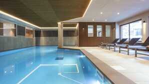Uma piscina interior moderna com água cristalina, cadeiras de descanso e vista para o exterior.