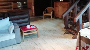 Interior de cabana de tronco com sofá, mesa pequena, cadeira de madeira e escada.