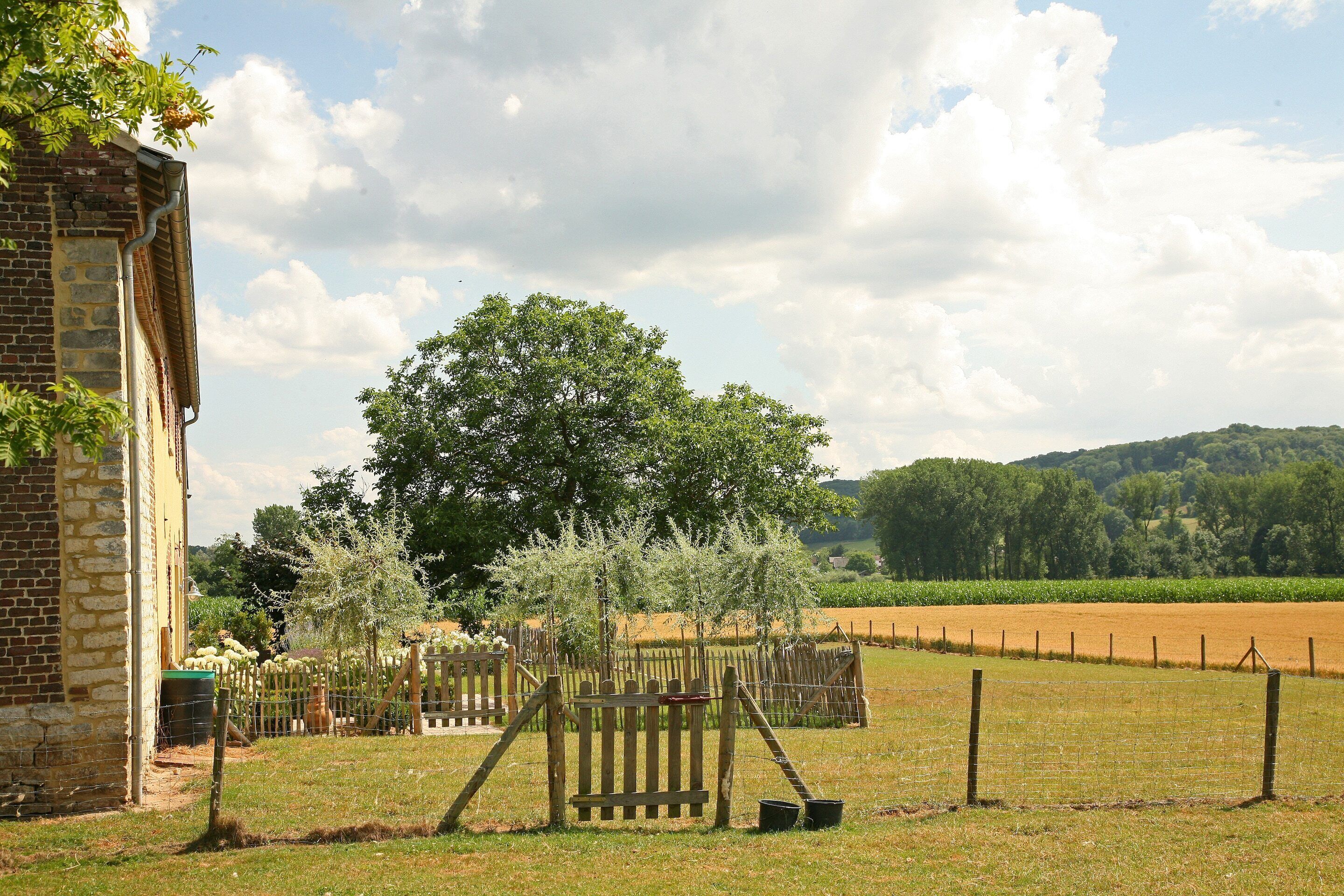 Een landelijk gelegen pand met een bakstenen gebouw, een omheinde tuin en een veld op de achtergrond.