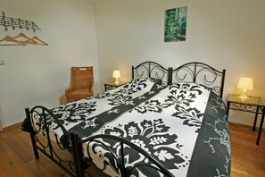 Una cama bien hecha con una colcha floral en blanco y negro, una silla y dos mesitas de noche con lámparas.