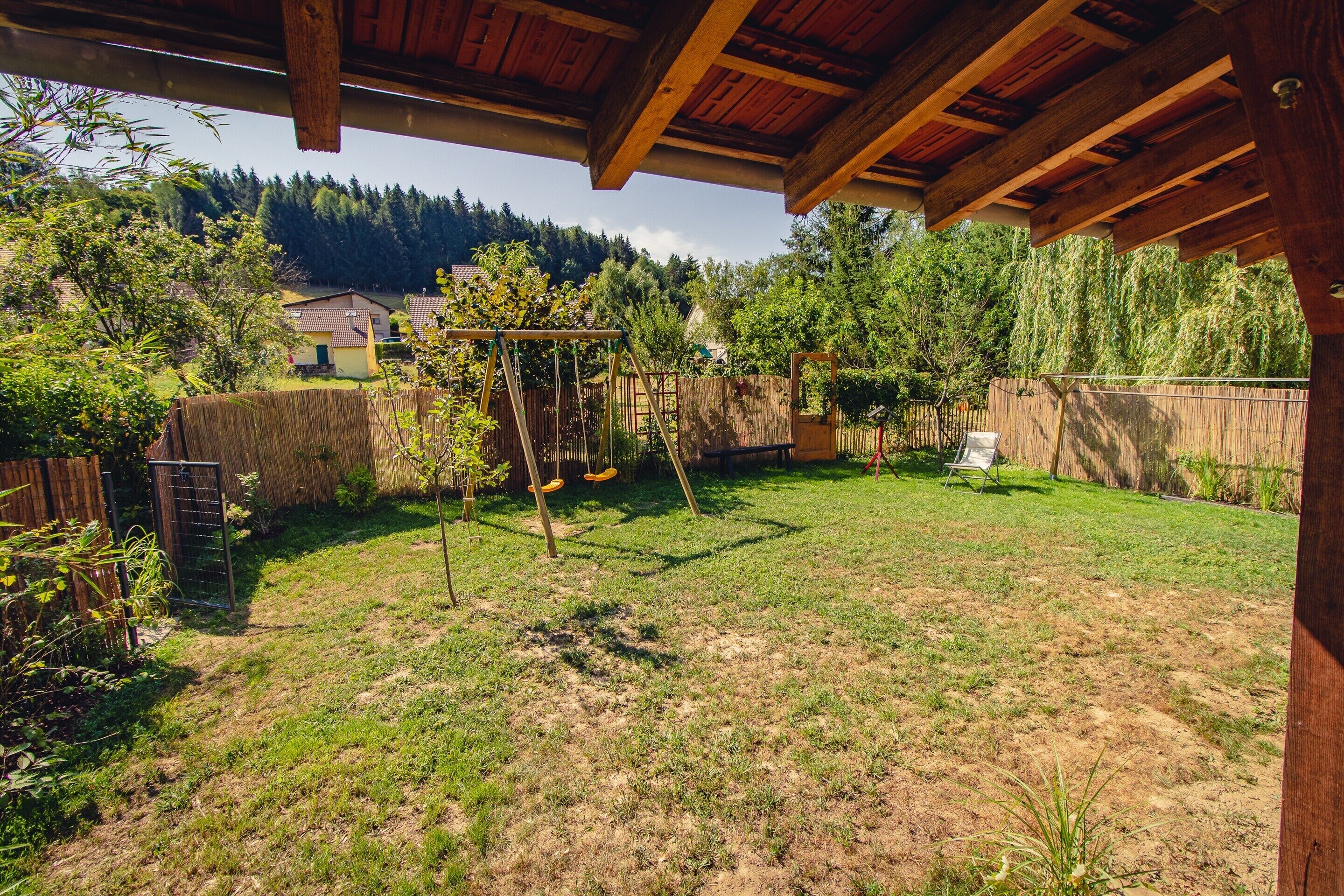 A backyard with a wooden pergola, a swing set, and a fenced area.