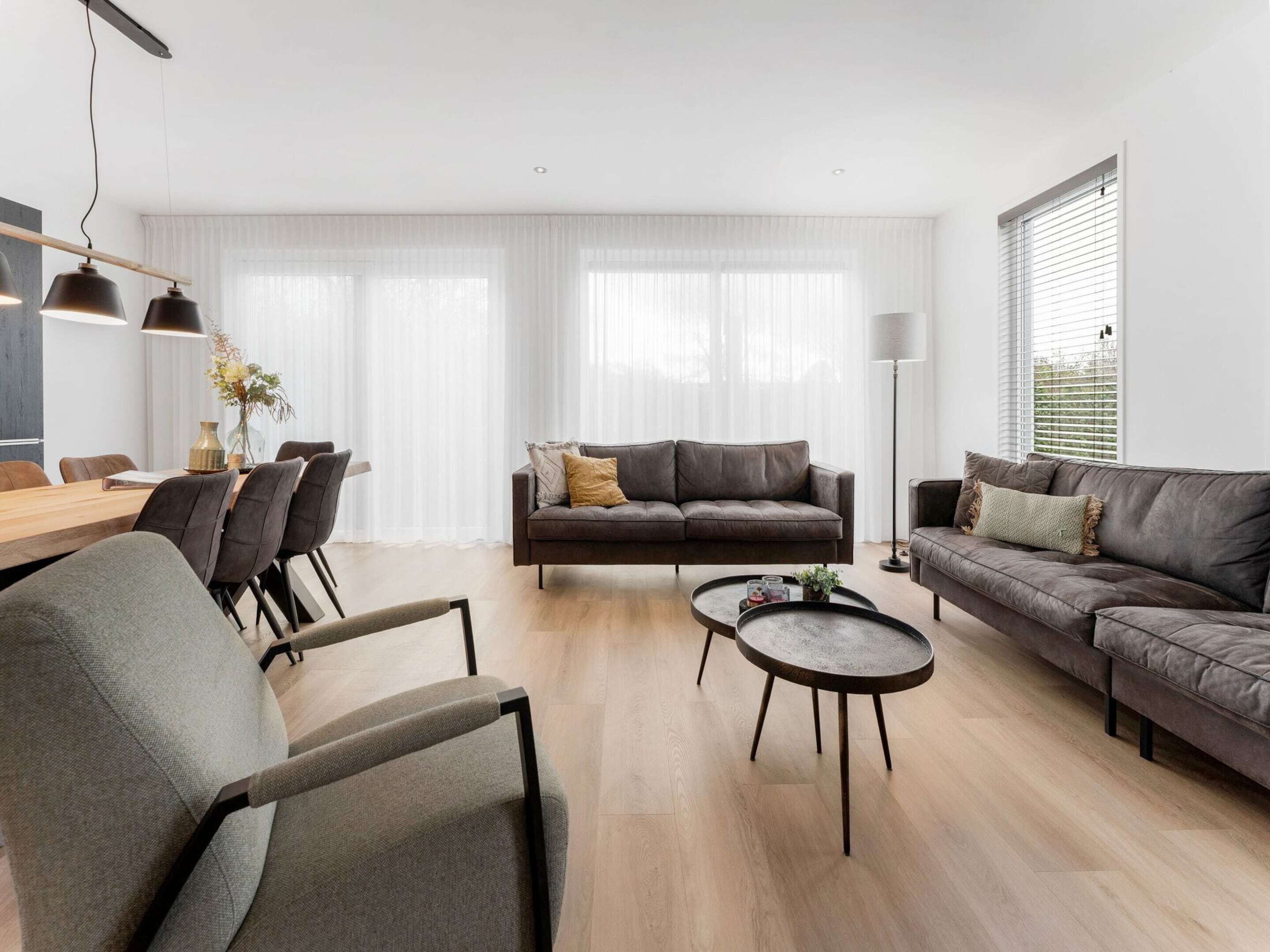 A modern living room with a sofa, armchairs, a coffee table, and a dining area with a table and chairs.