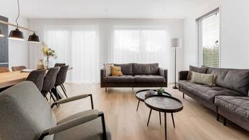 Ein modernes Wohnzimmer mit Sofa, Sesseln, einem Couchtisch und einem Essbereich mit Tisch und Stühlen.