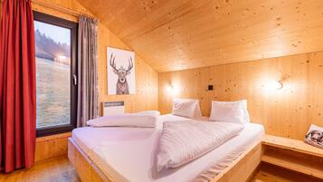 A wooden cabin room with a bed, a window with curtains, a wall-mounted light, and a framed picture.