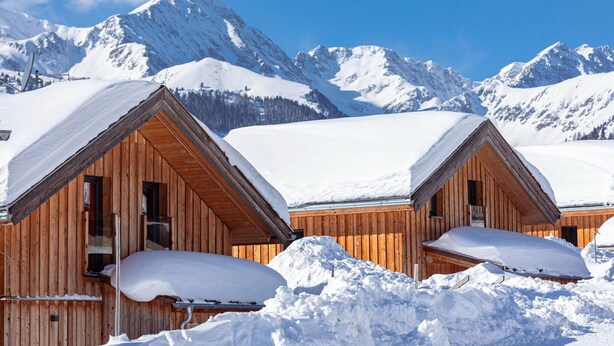 Two wooden cabins with pitched roofs, surrounded by snow, set against a backdrop of snow-covered mountains. - Chalet in Hohentauern With Sauna (Hohentauern)