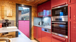 A modern kitchen with red cabinets, stainless steel appliances, and a wooden ceiling. - Chalet in Hohentauern With Sauna (Hohentauern)
