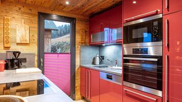 A modern kitchen with red cabinets, stainless steel appliances, and a wooden ceiling.
