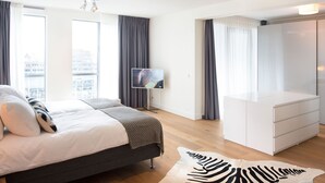 Una camera d'hotel moderna con un letto, una televisione, un armadio e un'ampia finestra con tende.