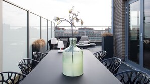 Una terrazza sul tetto con un tavolo lungo, sedie e un vaso con fiori.