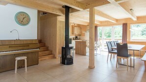 A spacious room with a wooden piano, a black stove, a dining area with chairs, and a kitchen in the background. - Spectacular Chalet near Ski Area in Sankt Georgen ob Murau (Sankt Georgen am Kreischberg)