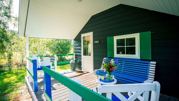 Eine überdachte Veranda mit Holzterrasse, einer Bank und einem kleinen Tisch mit Blumen in einer Vase.