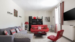 Un salon avec un canapé gris, un canapé rouge, un fauteuil rouge, une table basse noire et un téléviseur à écran plat fixé au mur.