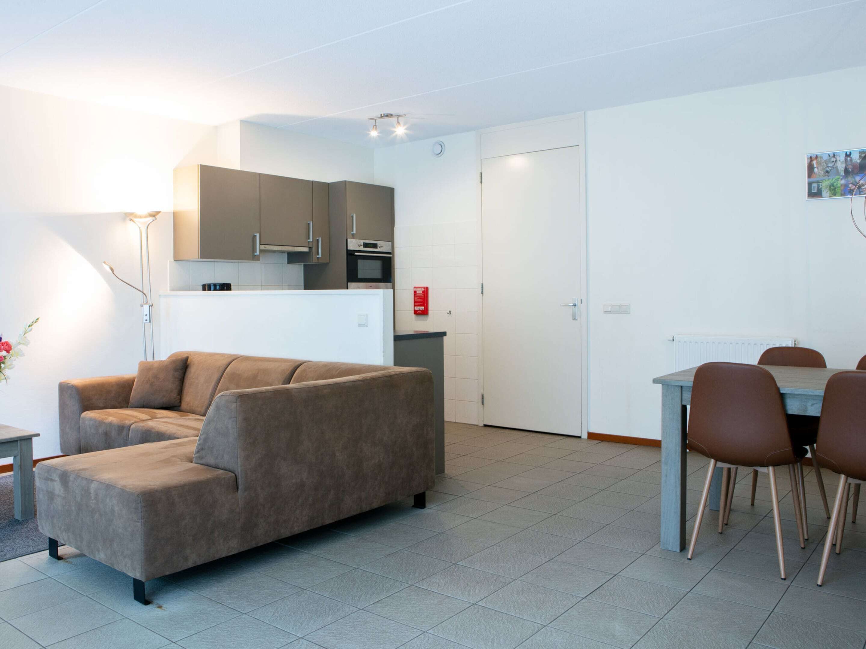 Una sala de estar moderna con sofá, una mesa de comedor con sillas, una zona de cocina con armarios y una puerta blanca.