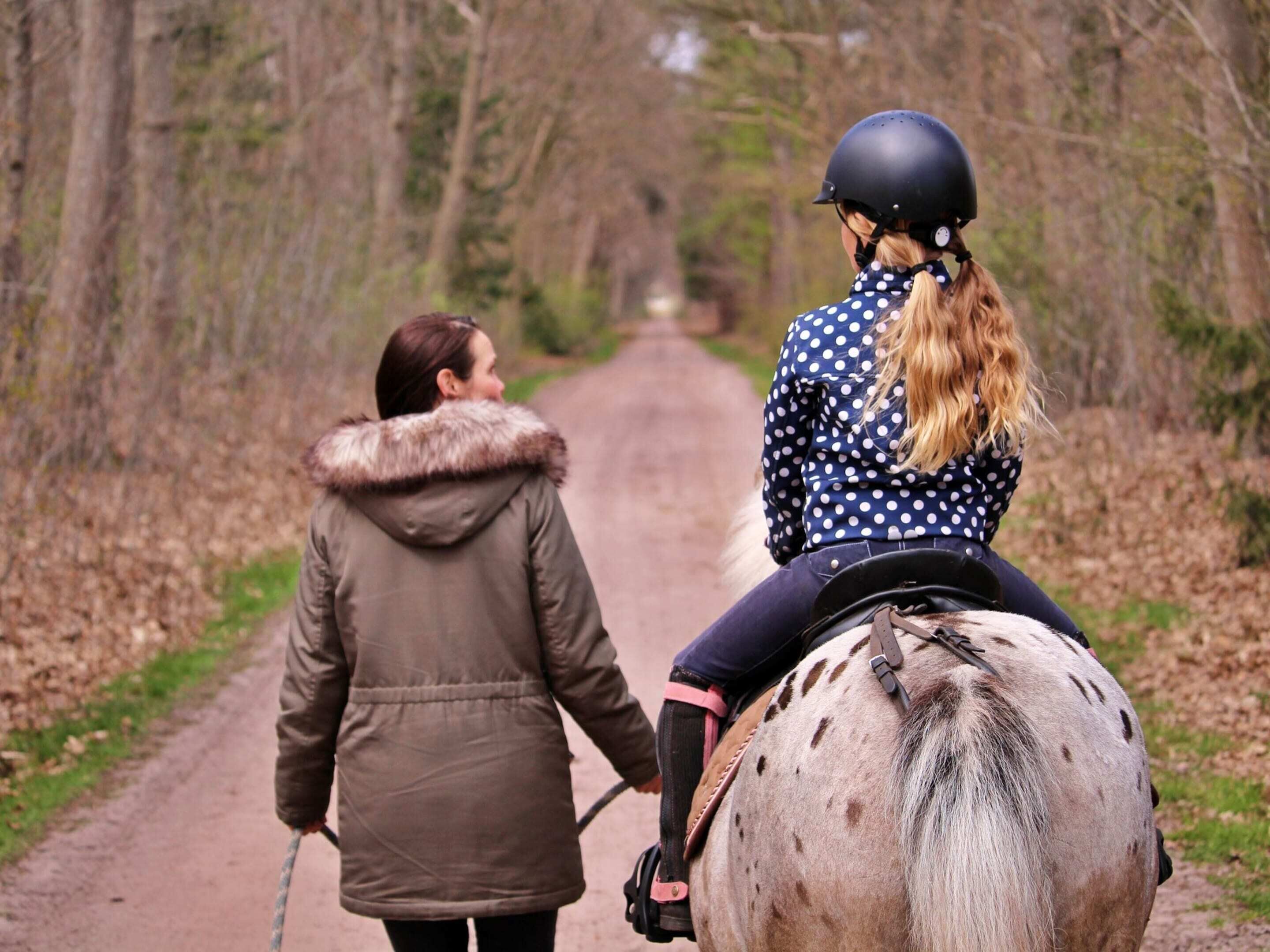 Two people riding a horse on a paved path surrounded by trees.