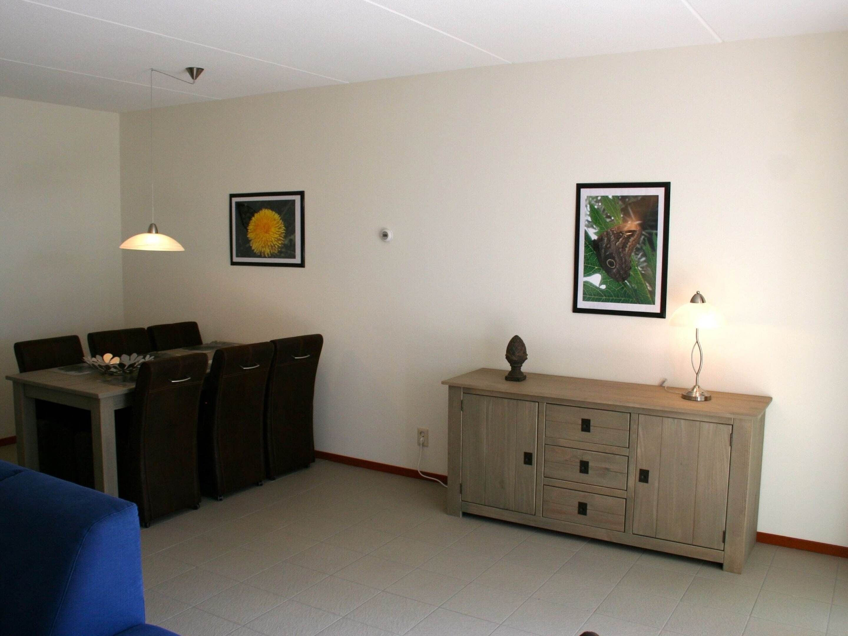 A dining area with a table, chairs, a cabinet, and two wall-mounted lamps.