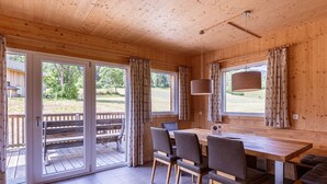 Una cabaña de madera con comedor, una banca afuera y vistas del exterior.