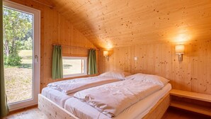 Un dormitorio de cabaña de madera con dos camas, una ventana con cortinas y una lámpara fijada a la pared.