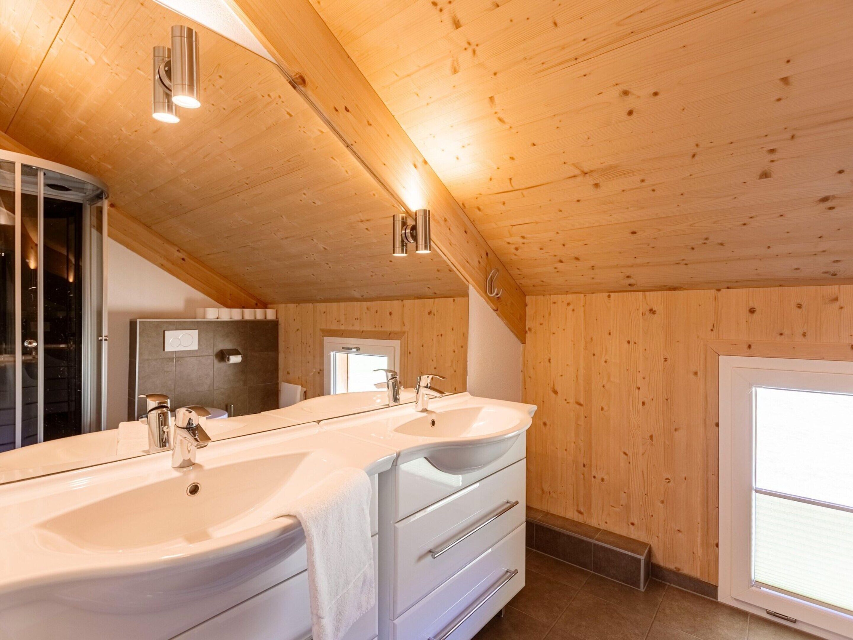 Un baño moderno con paneles de madera, un espejo grande, dos lavamanos y una zona de ducha.