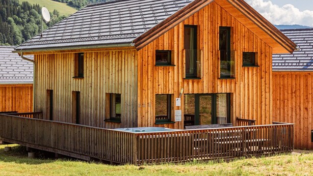 Una cabaña de madera con techo inclinado, ventanas grandes y una terraza de madera.