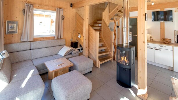A cozy wooden cabin interior with a sofa, ottoman, staircase, and a wood-burning stove. - Beautiful Chalet With hot tub (Sankt Georgen am Kreischberg)