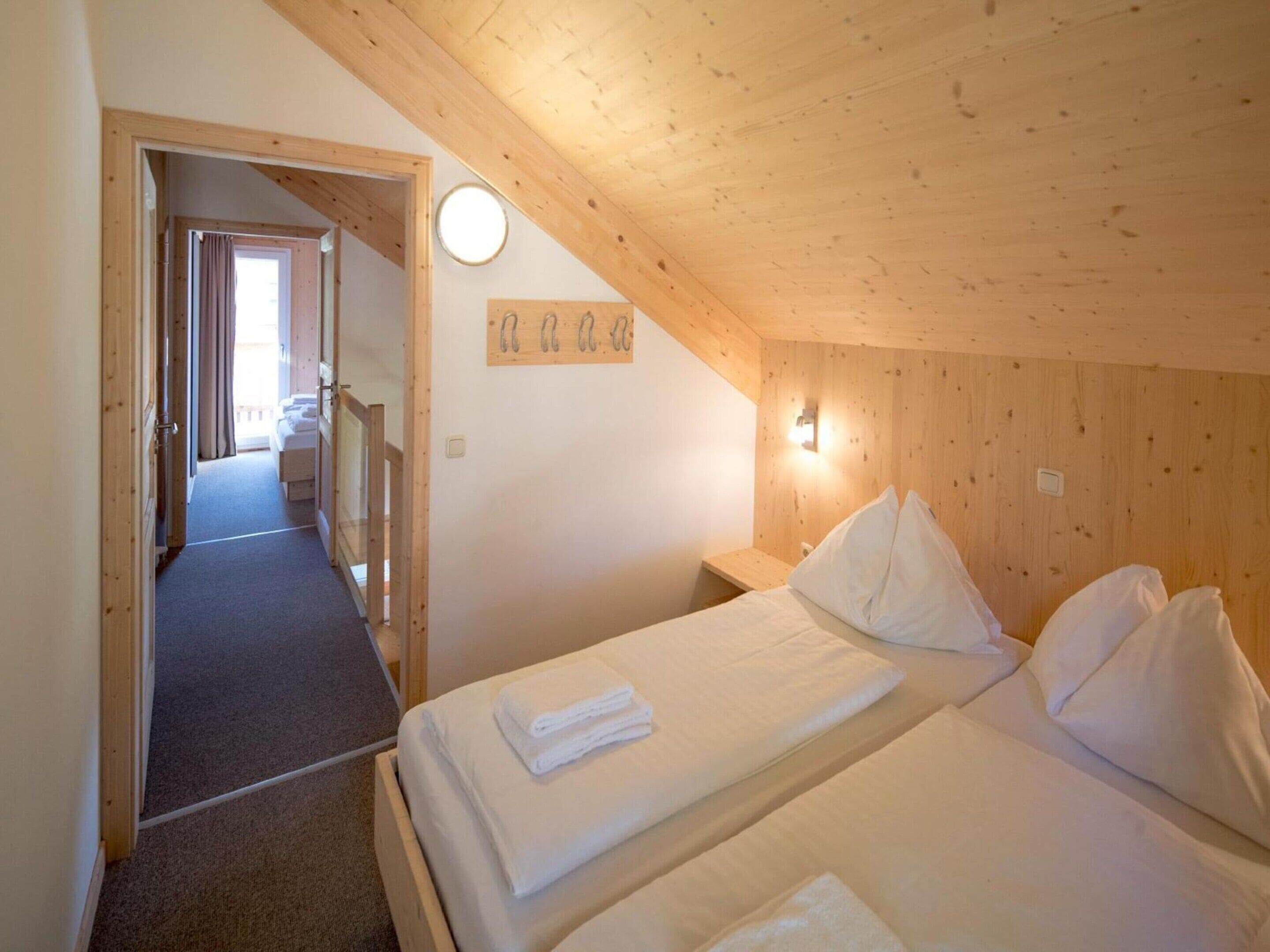 A bedroom with two beds, wooden walls, a small bedside table, and a light fixture.