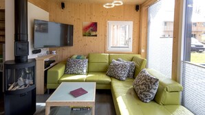 A cozy living room with a green sofa, a flat-screen TV, a fireplace, and a window with a view. - Attractive Chalet With hot tub (Sankt Georgen am Kreischberg)
