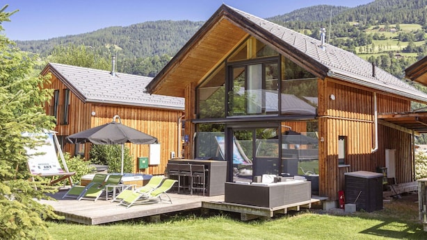 A wooden cabin with a large glass extension, outdoor seating, and a view of a mountainous landscape. - Attractive Chalet With hot tub (Sankt Georgen am Kreischberg)